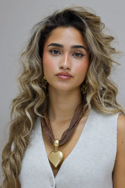 bruine gevlochten ketting met groot goud hart plat gelegd op witte ondergrond