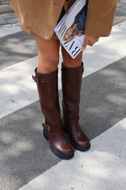 Model draagt bruine laarzen met gespen buiten op straat