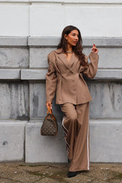 Model loopt op straat in bruine oversized blazer en wijde pantalon