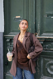 model draagt bruine satijnen top met kanten rand en blazer buiten met koffie in hand