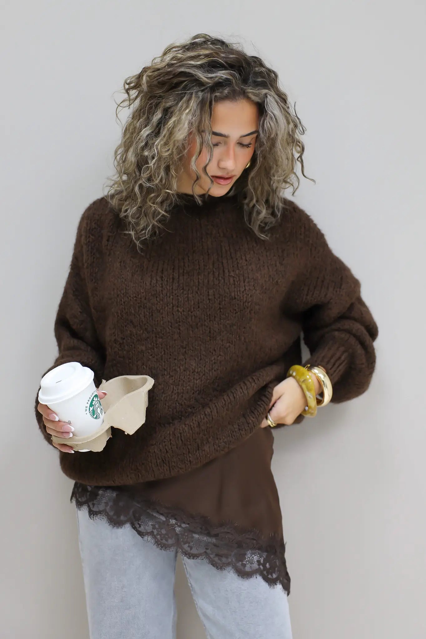 model draagt gebreide bruine trui over satijnen top met kanten details