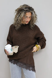 model draagt gebreide bruine trui over satijnen top met kanten details