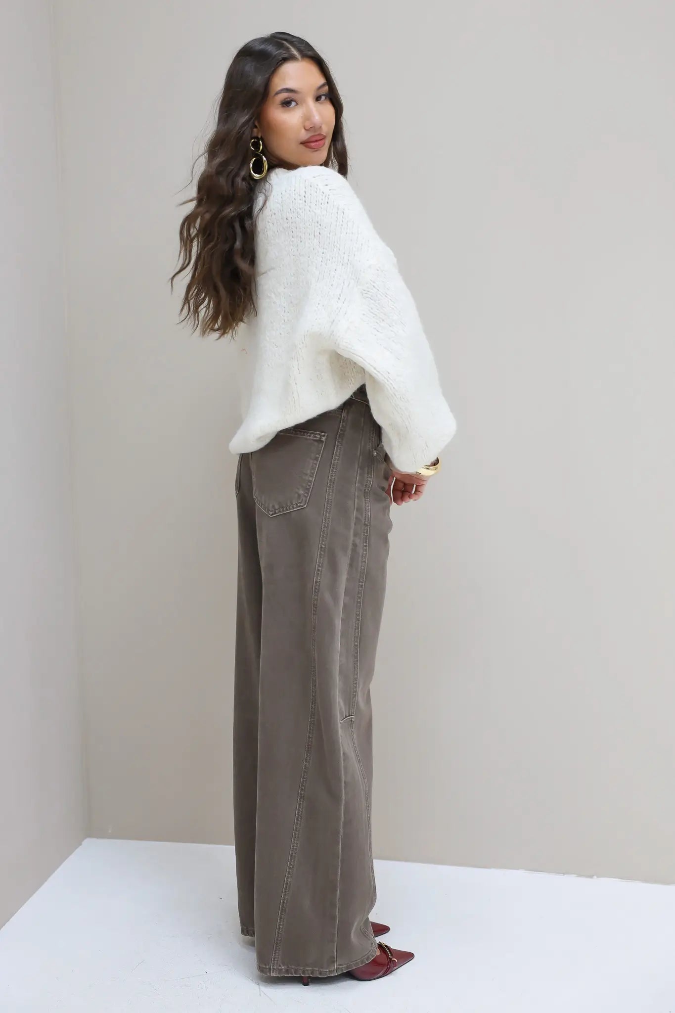 Model draait zich om in witte trui en bruine wide leg jeans