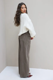 Model draait zich om in witte trui en bruine wide leg jeans