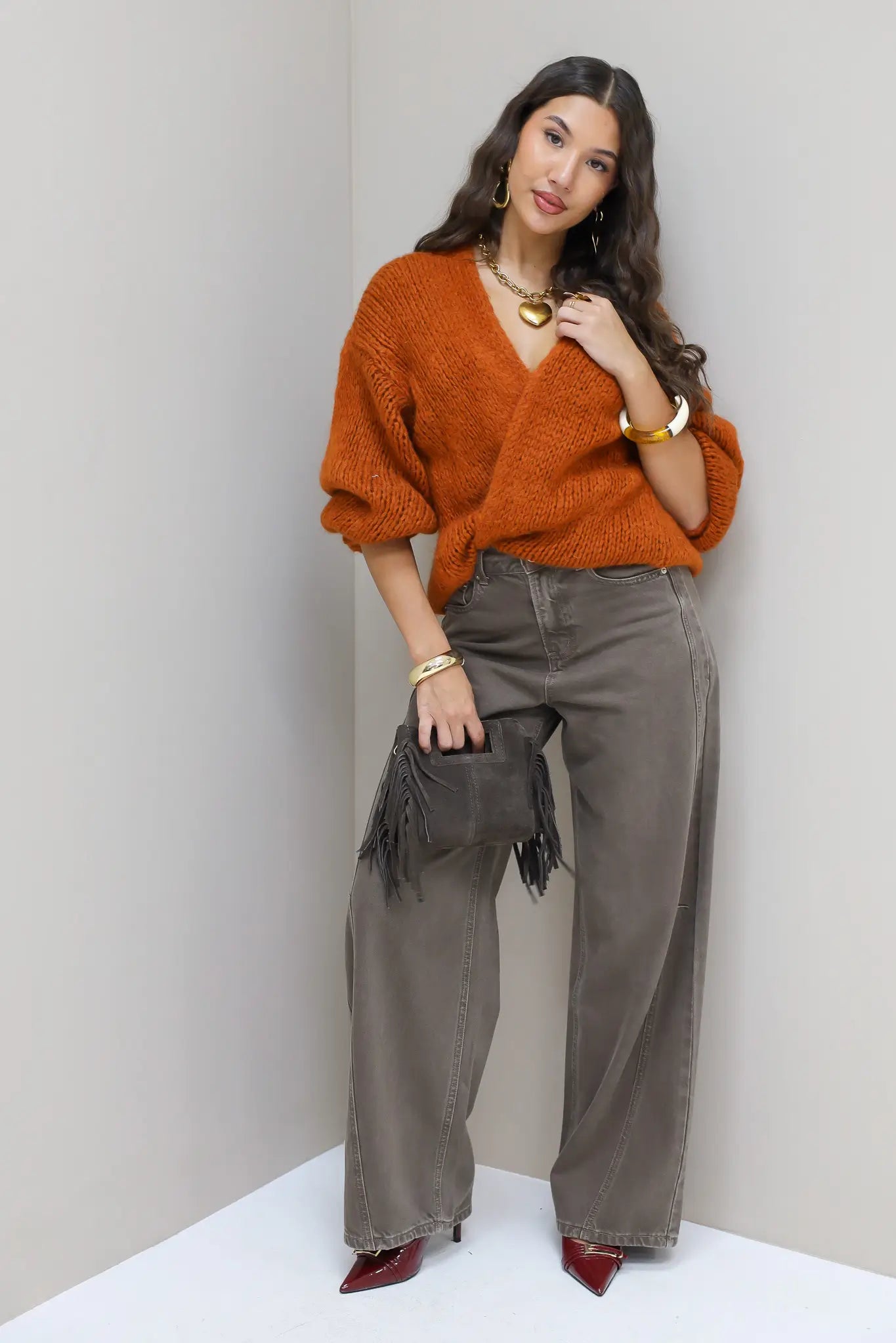 Model draagt bruine wide leg jeans met oranje trui en handtas