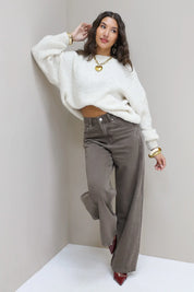 Model poseert in witte trui met bruine wide leg jeans tegen muur