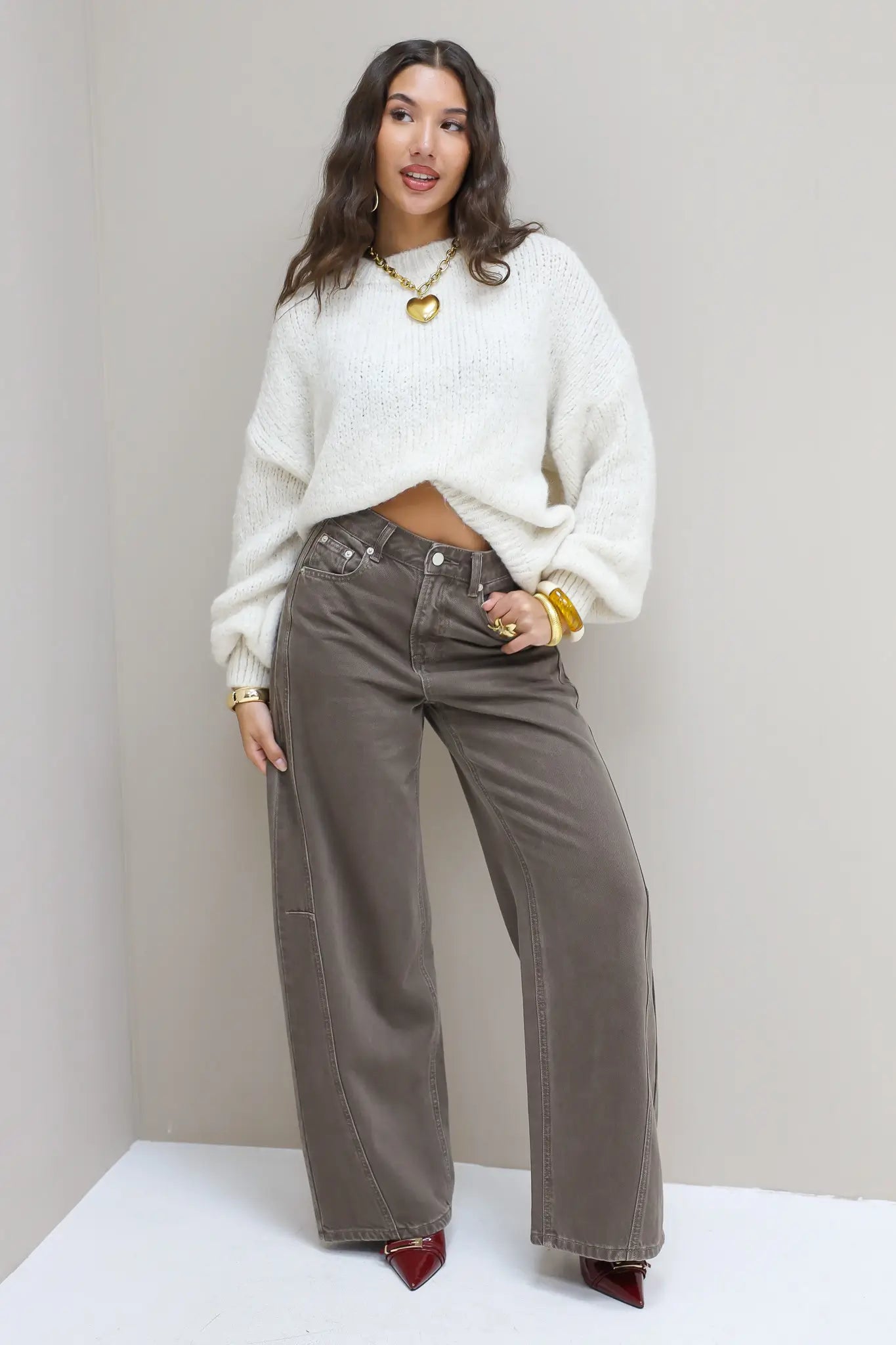 Model draagt bruine wide leg jeans met witte trui en hakken
