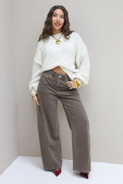 Model draagt bruine wide leg jeans met witte trui en hakken