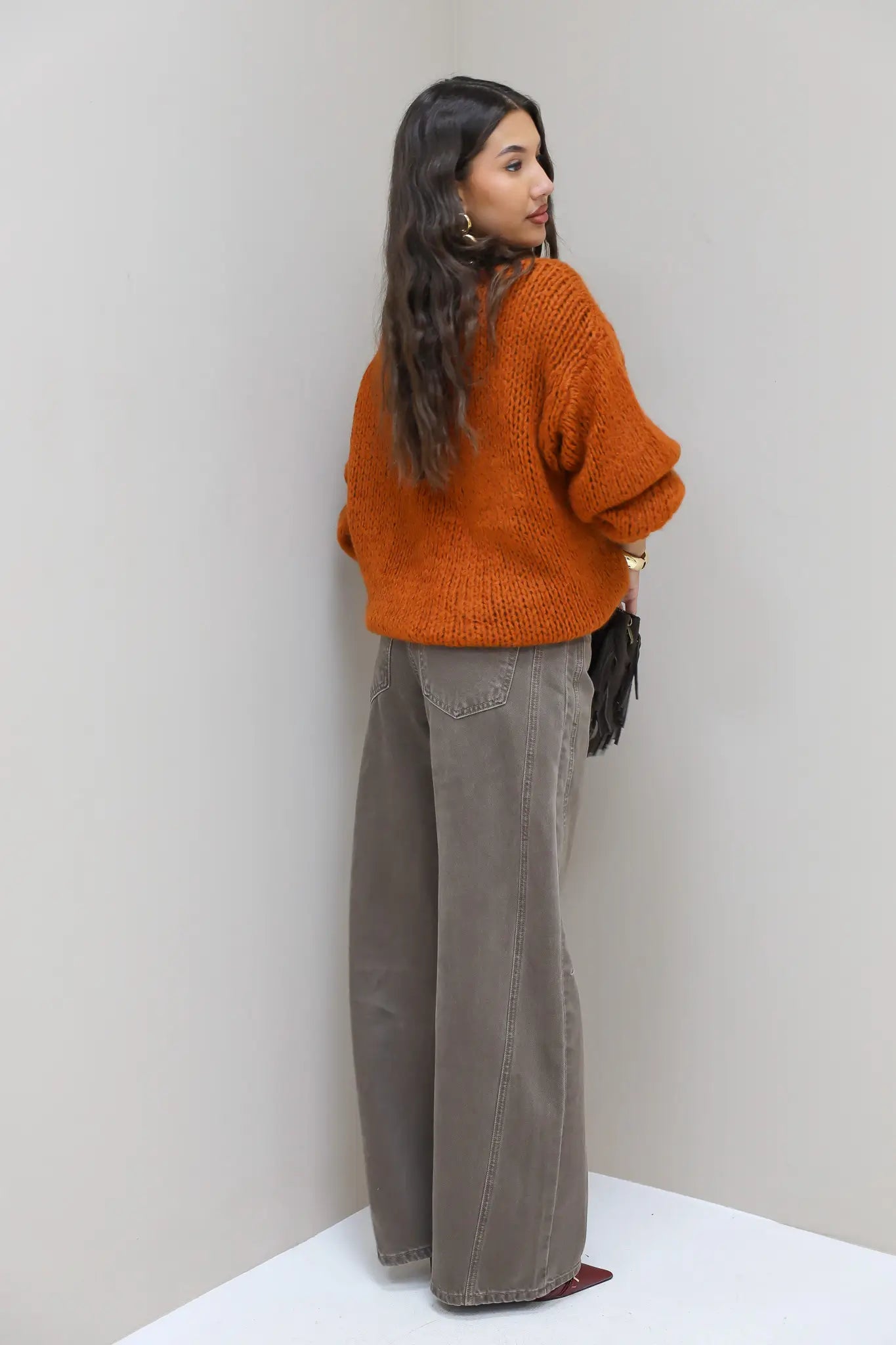 Model in bruine wide leg jeans en oranje trui, gezien vanaf de zijkant