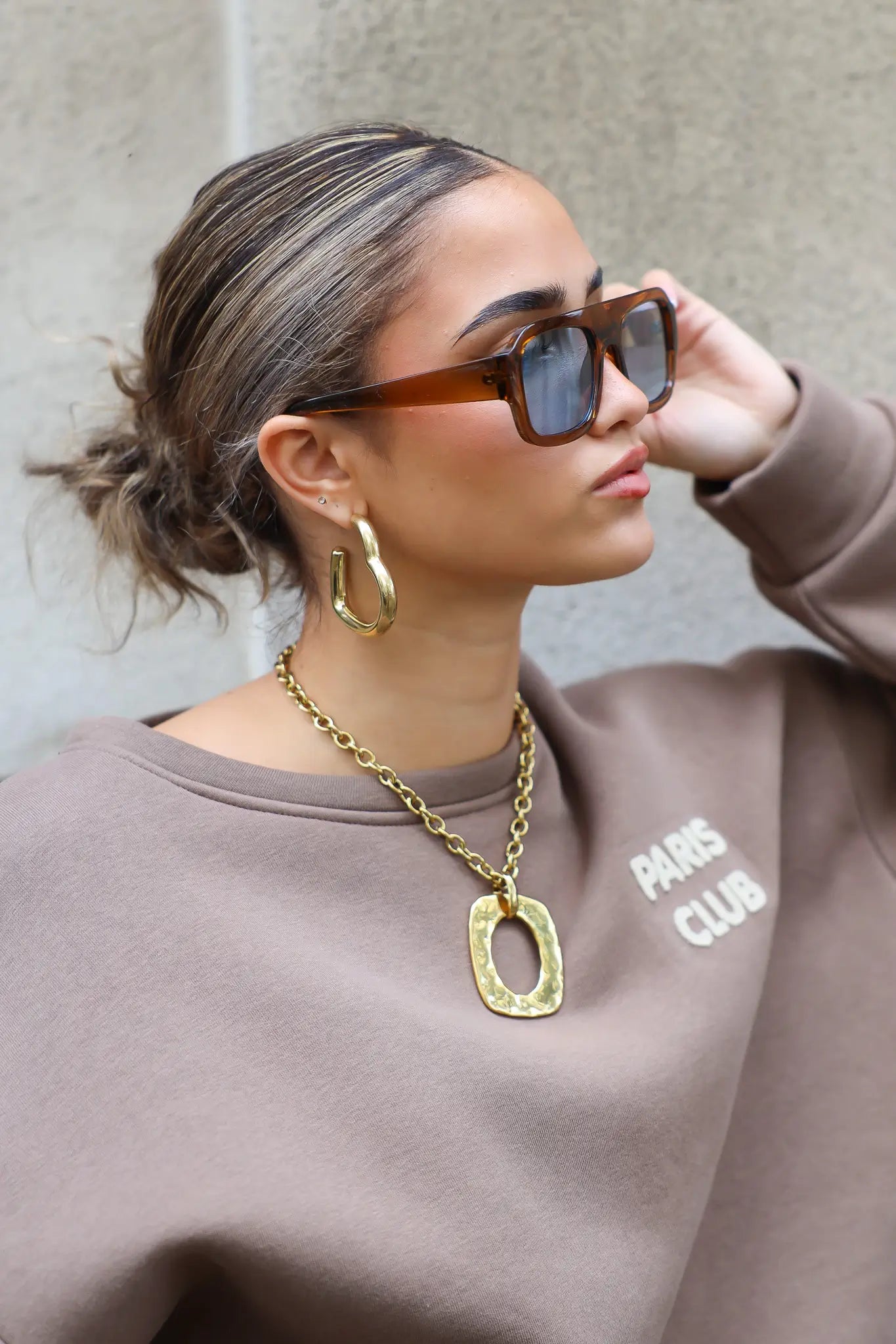 close-up van model met bruine zonnebril, gouden ketting en trui met Paris Club logo