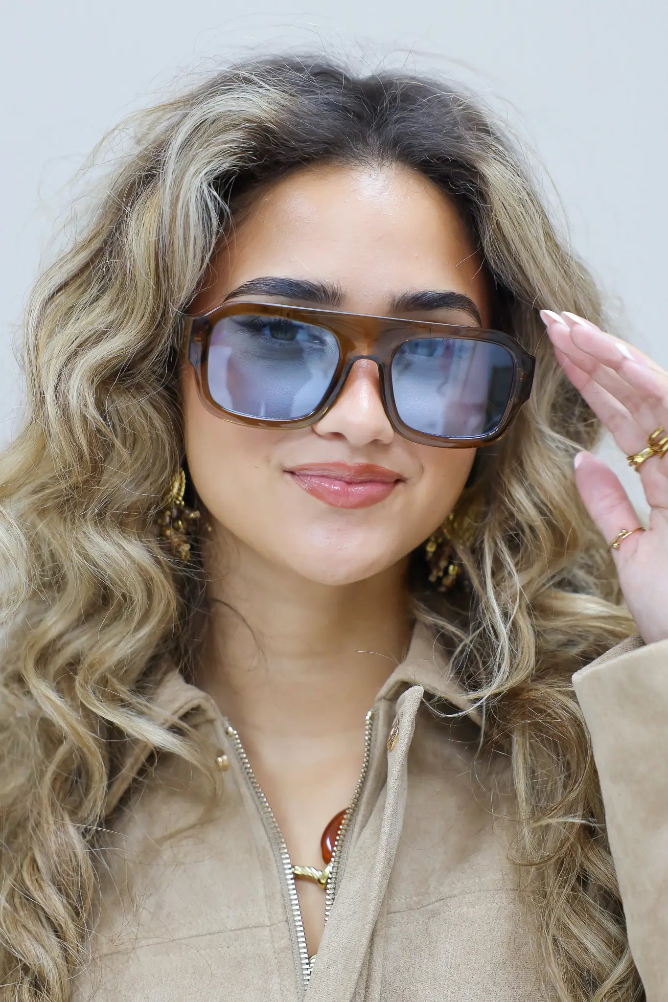 model met bruine zonnebril kijkt recht vooruit met beige outfit