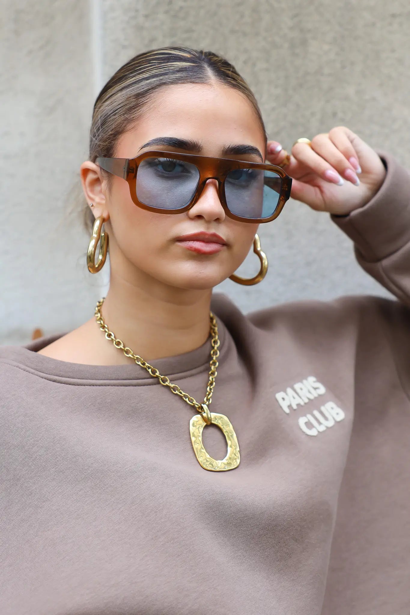 model met zonnebril houdt haar hand bij de bril en kijkt richting camera