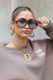 model met zonnebril houdt haar hand bij de bril en kijkt richting camera