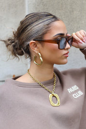 model met zonnebril kijkt opzij, haar in een lage knot en gouden oorbellen zichtbaar