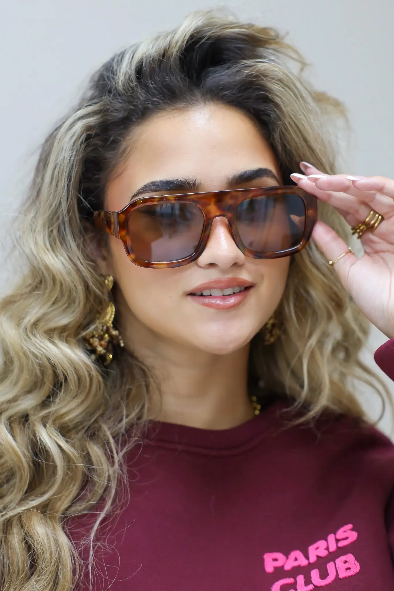 model met zonnebril kijkt opzij met golvend haar en bordeaux trui