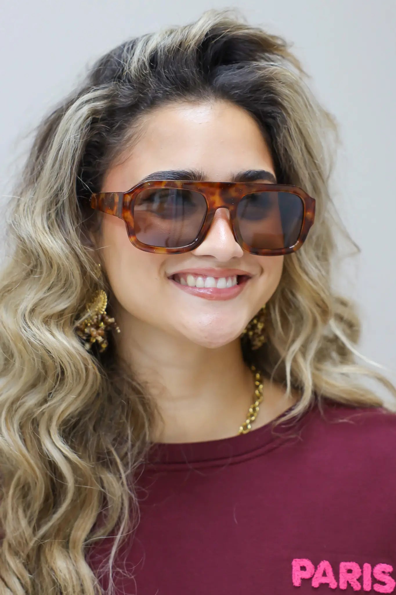 close-up van model met bruine zonnebril, hand bij gezicht, bordeaux top goed zichtbaar