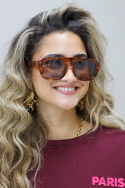 close-up van model met bruine zonnebril, hand bij gezicht, bordeaux top goed zichtbaar