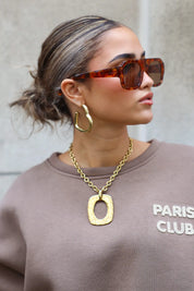 close-up van model met bruine zonnebril en gouden ketting tegen grijze muur