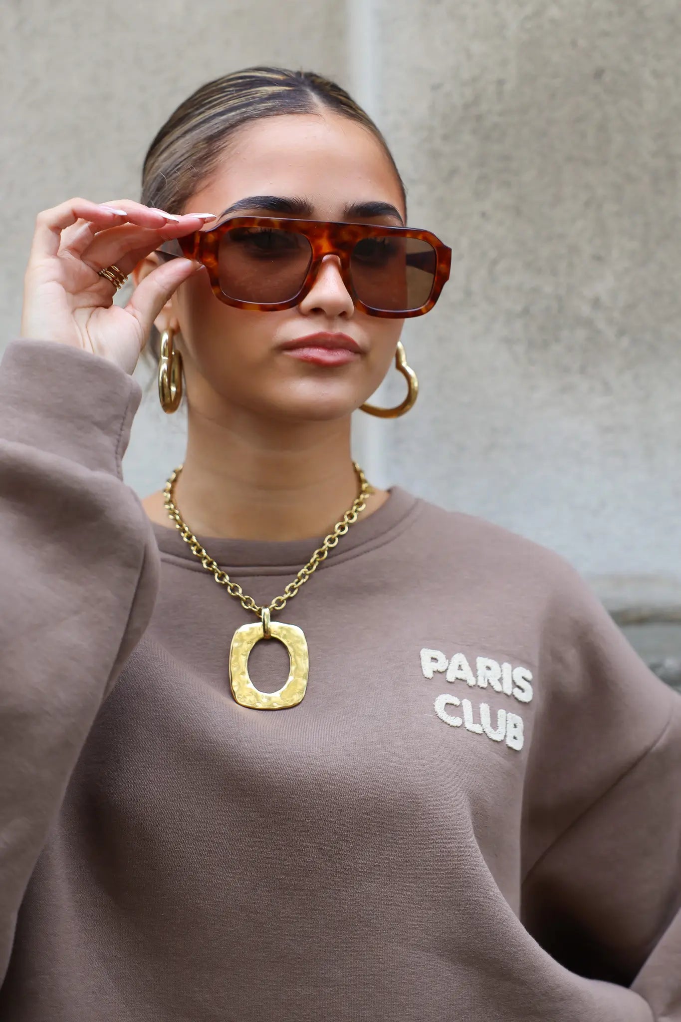 model met bruine zonnebril kijkt recht vooruit en draagt trui met opdruk Paris Club