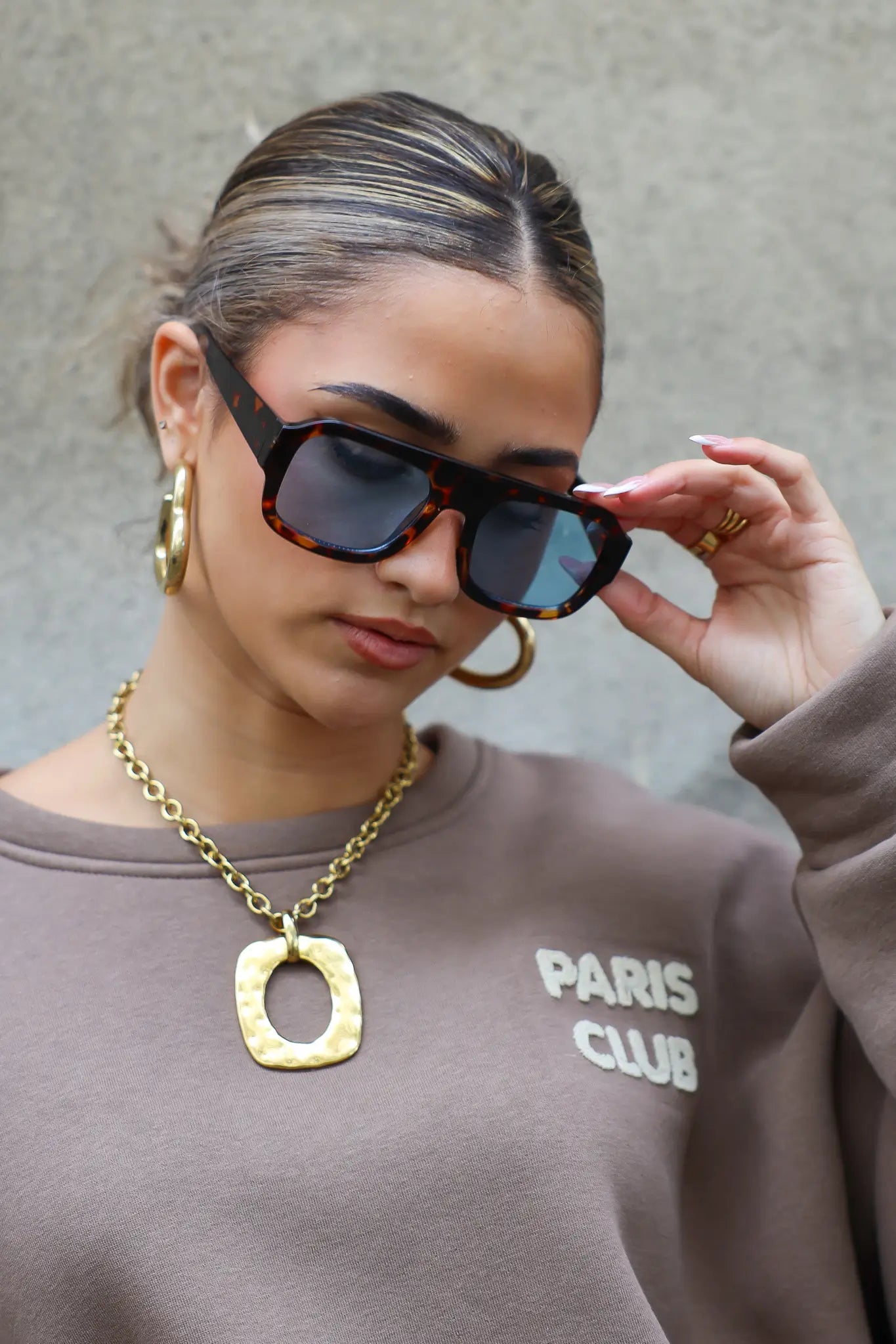 model met bruine zonnebril kijkt opzij en draagt een trui met opdruk Paris Club