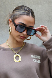 model met bruine zonnebril kijkt opzij en draagt een trui met opdruk Paris Club