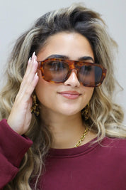 model met bruine zonnebril kijkt recht vooruit met los vallend haar