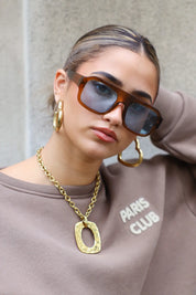 model met zonnebril kijkt omlaag met hand in het haar, ketting goed zichtbaar