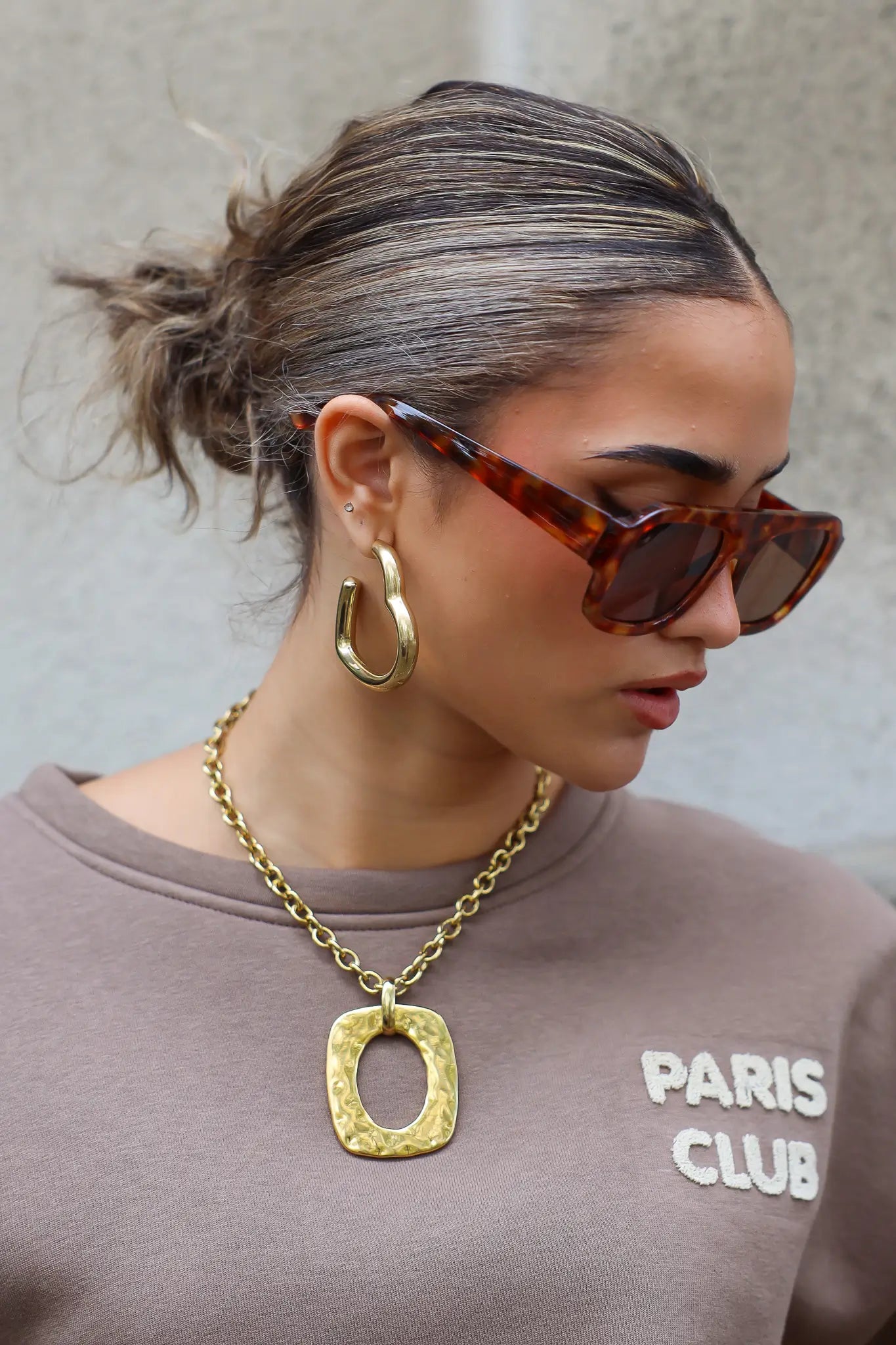 zijaanzicht van model met bruine zonnebril en grote oorbel