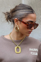 zijaanzicht van model met bruine zonnebril en grote oorbel