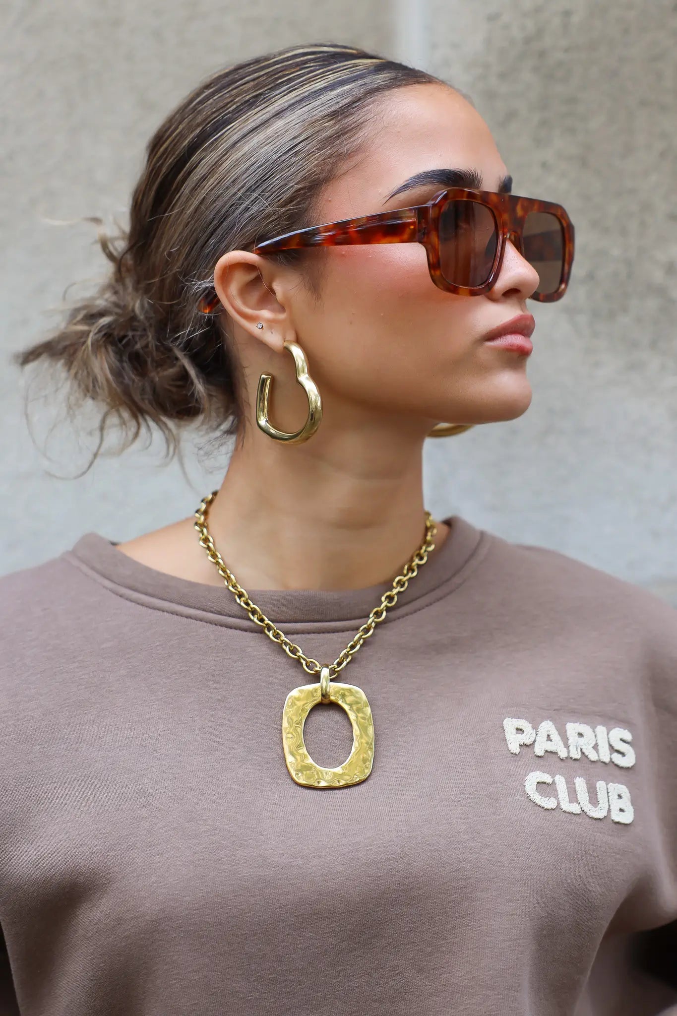 model met bruine zonnebril kijkt opzij, haar in knot, ketting goed zichtbaar