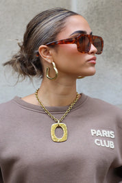 model met bruine zonnebril kijkt opzij, haar in knot, ketting goed zichtbaar