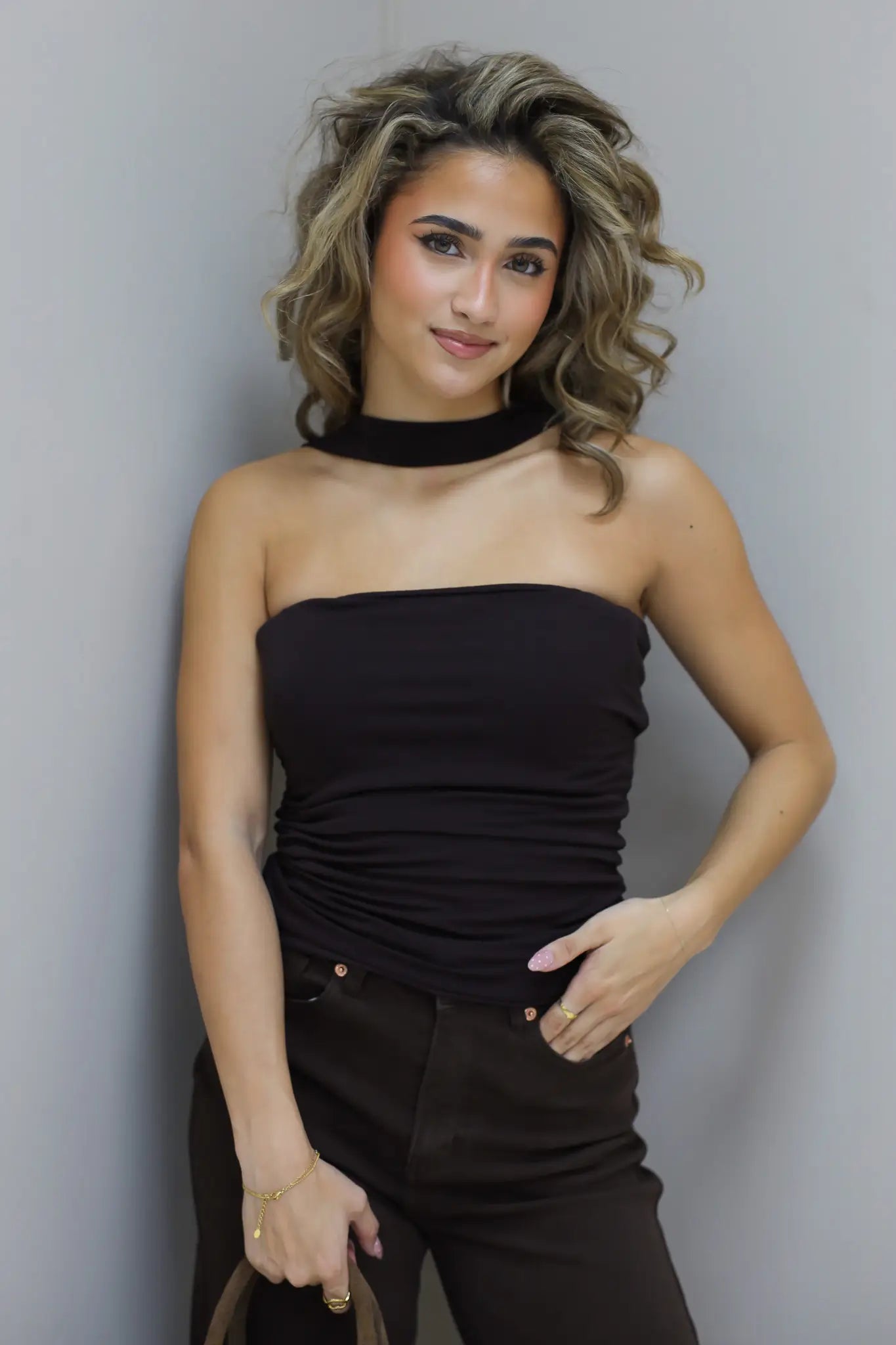 Model draagt bruine choker top met hand in broekzak en neutrale blik