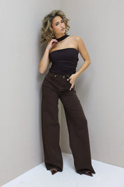 Model draagt choker top met hand in zak en glimlacht zacht richting camera