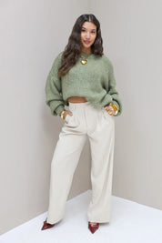 Model draagt crèmekleurige pantalon met groene trui en hakken