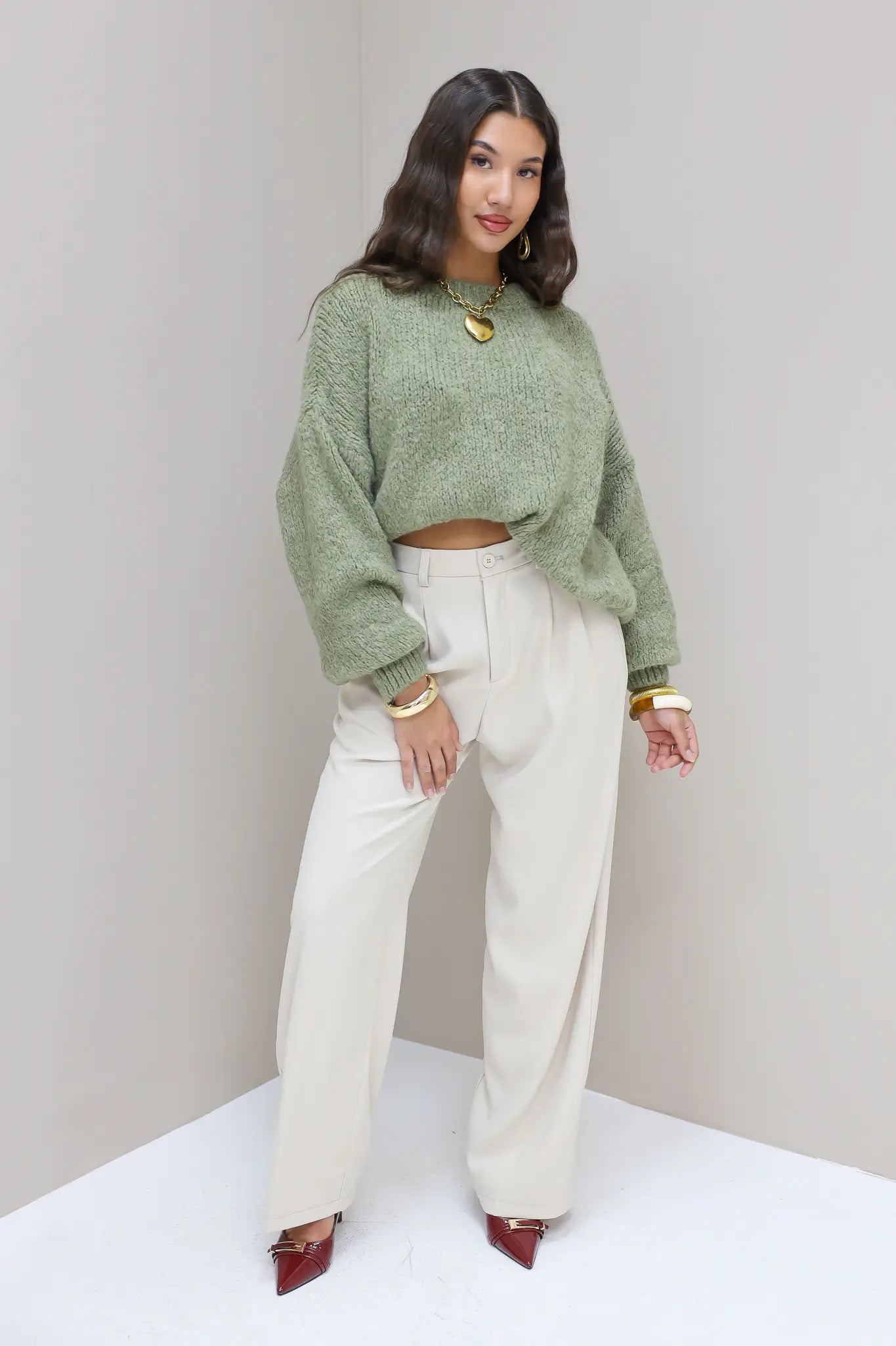 Model staat bij muur met cremekleurige pantalon en groene trui