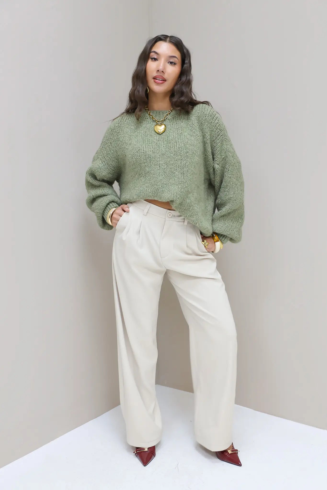 Model poseert recht in cremekleurige pantalon en groene trui