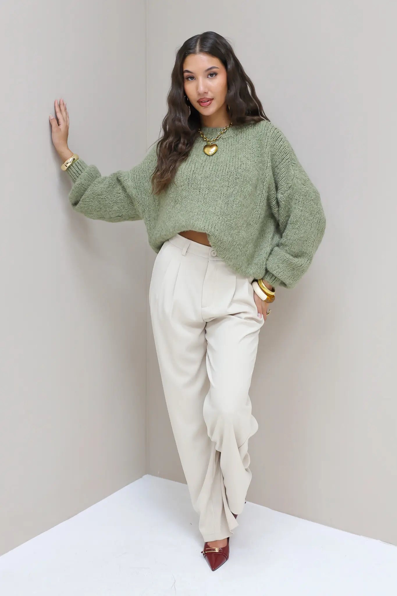 Model zet stap voorwaarts in cremekleurige pantalon en groene trui