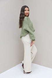Model in cremekleurige pantalon met groene trui vanaf de zijkant