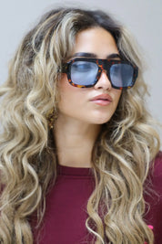 close-up van model met blauwe zonnebril en los haar, kijkt licht schuin richting camera