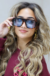 model met donkerblauwe zonnebril kijkt recht vooruit met los haar en bordeaux top