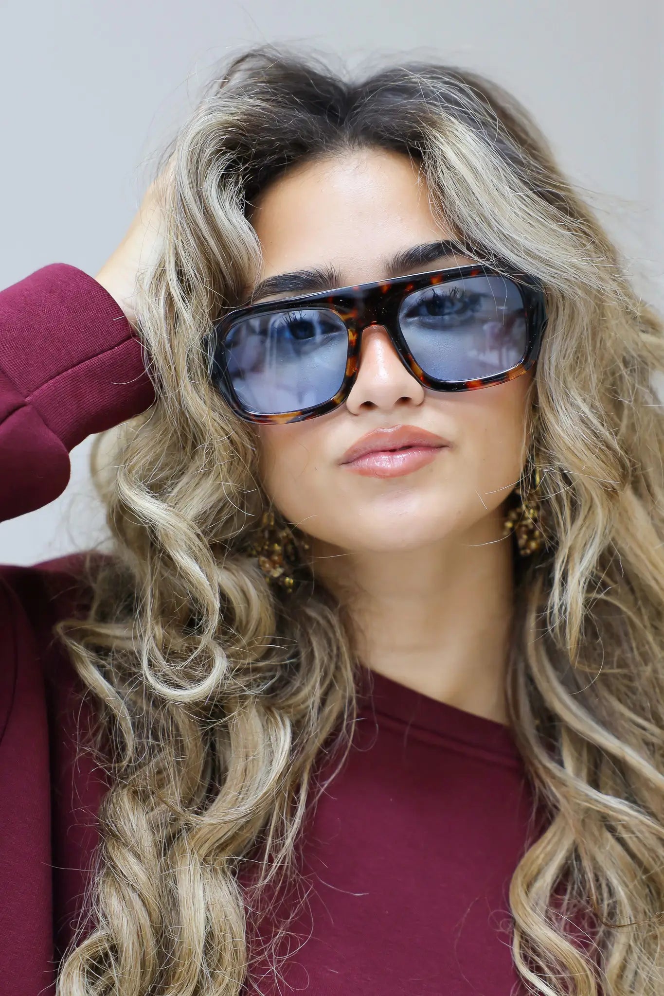 model met blauwe zonnebril raakt haar bril aan en kijkt richting camera