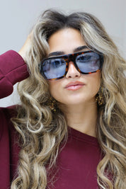 model met blauwe zonnebril raakt haar bril aan en kijkt richting camera