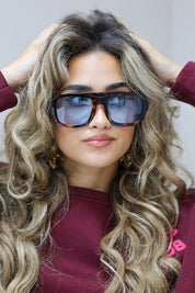 model met blauwe zonnebril en golvend haar kijkt iets omhoog in bordeaux top