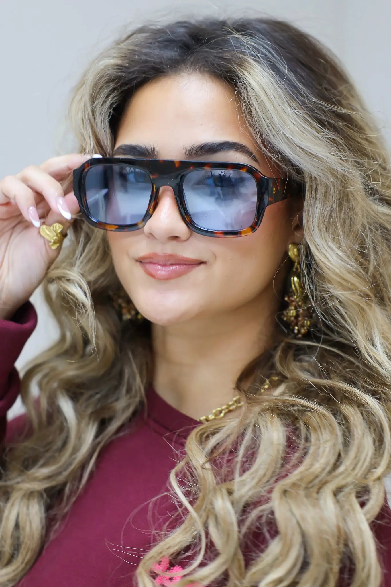 model met blauwe zonnebril kijkt recht vooruit met hand in het haar