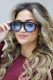 model met blauwe zonnebril kijkt recht vooruit met hand in het haar