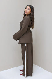 Model kijkt schuin over schouder in donkerbruine blazer met pantalon met witte bies