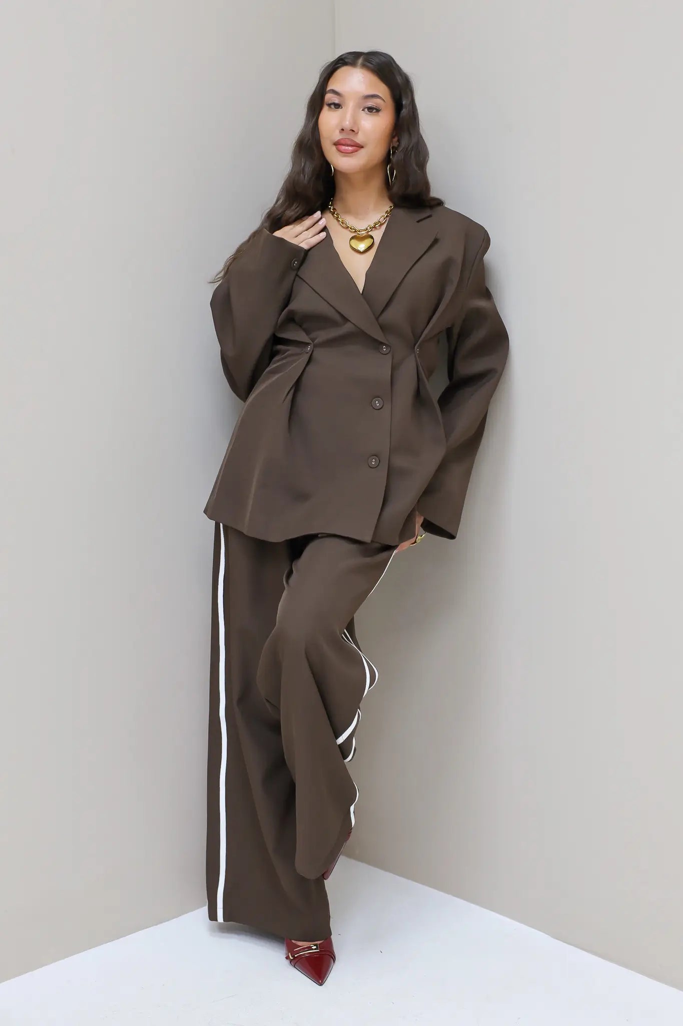 Model met donkerbruine blazer en pantalon met witte bies, frontaal gefotografeerd