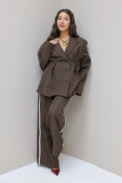 Model met donkerbruine blazer en pantalon met witte bies, frontaal gefotografeerd