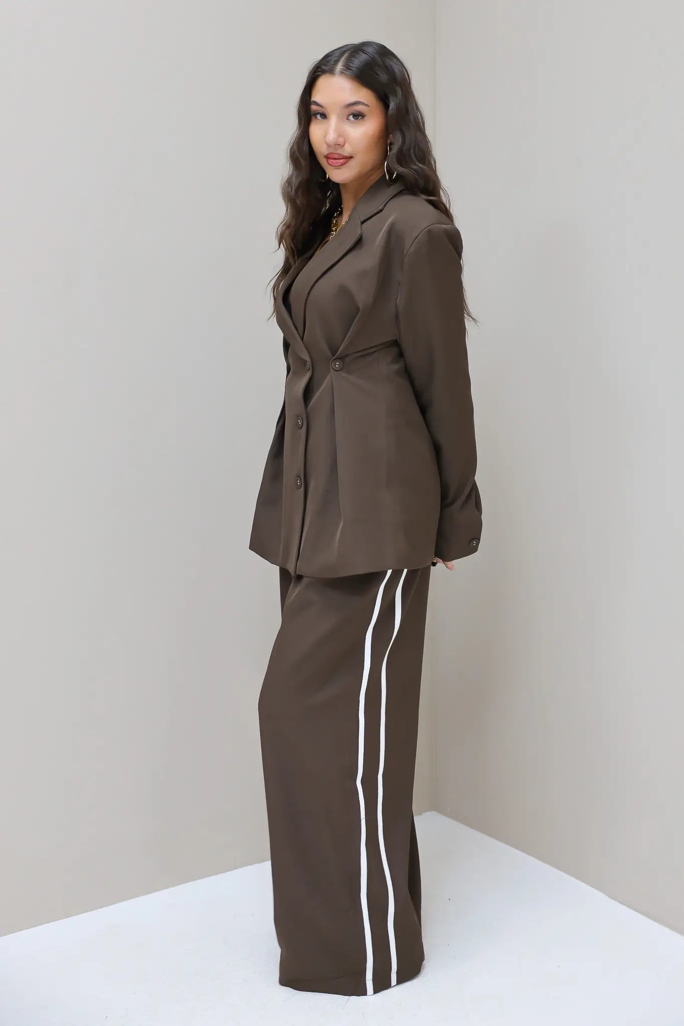 Model in donkerbruine blazer met pantalon met witte bies, gezien vanaf de zijkant