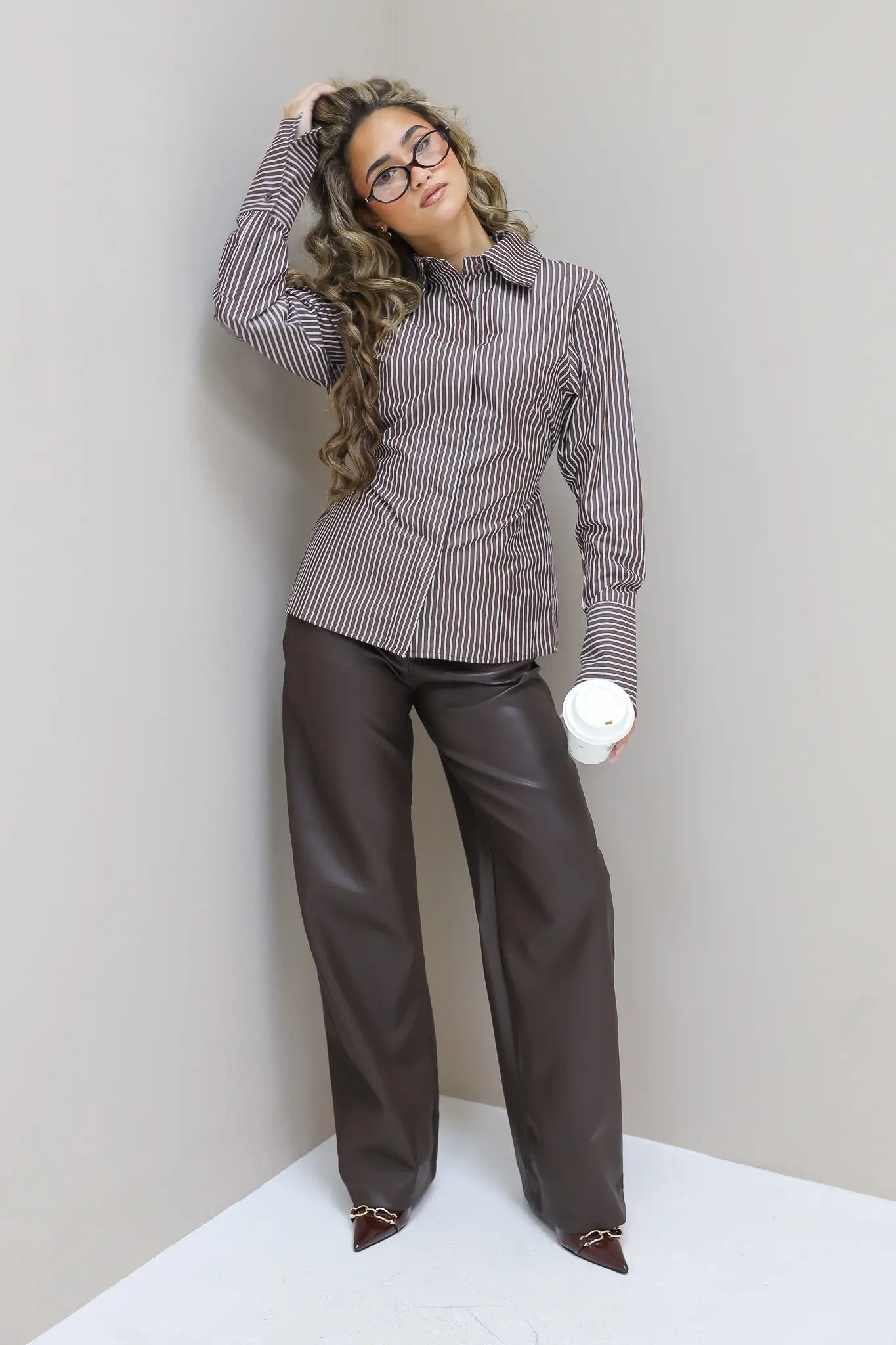 Model met fur jas en faux leather broek, tegen beige muur, handen in zakken